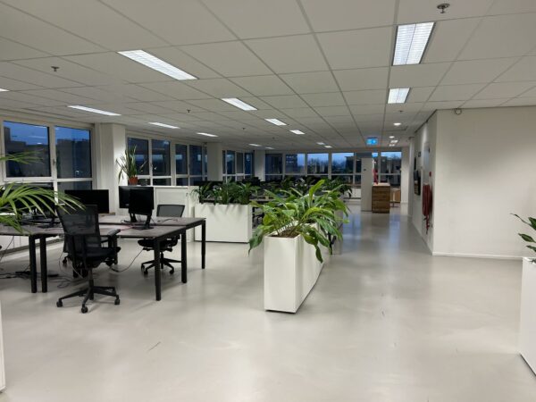 Modern open kantoorinterieur in Rivium Quadrant met bureaus, computers en veel groene planten.